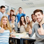 Viele glückliche Studenten halten Daumen hoch mit dem Dozent in der Uni